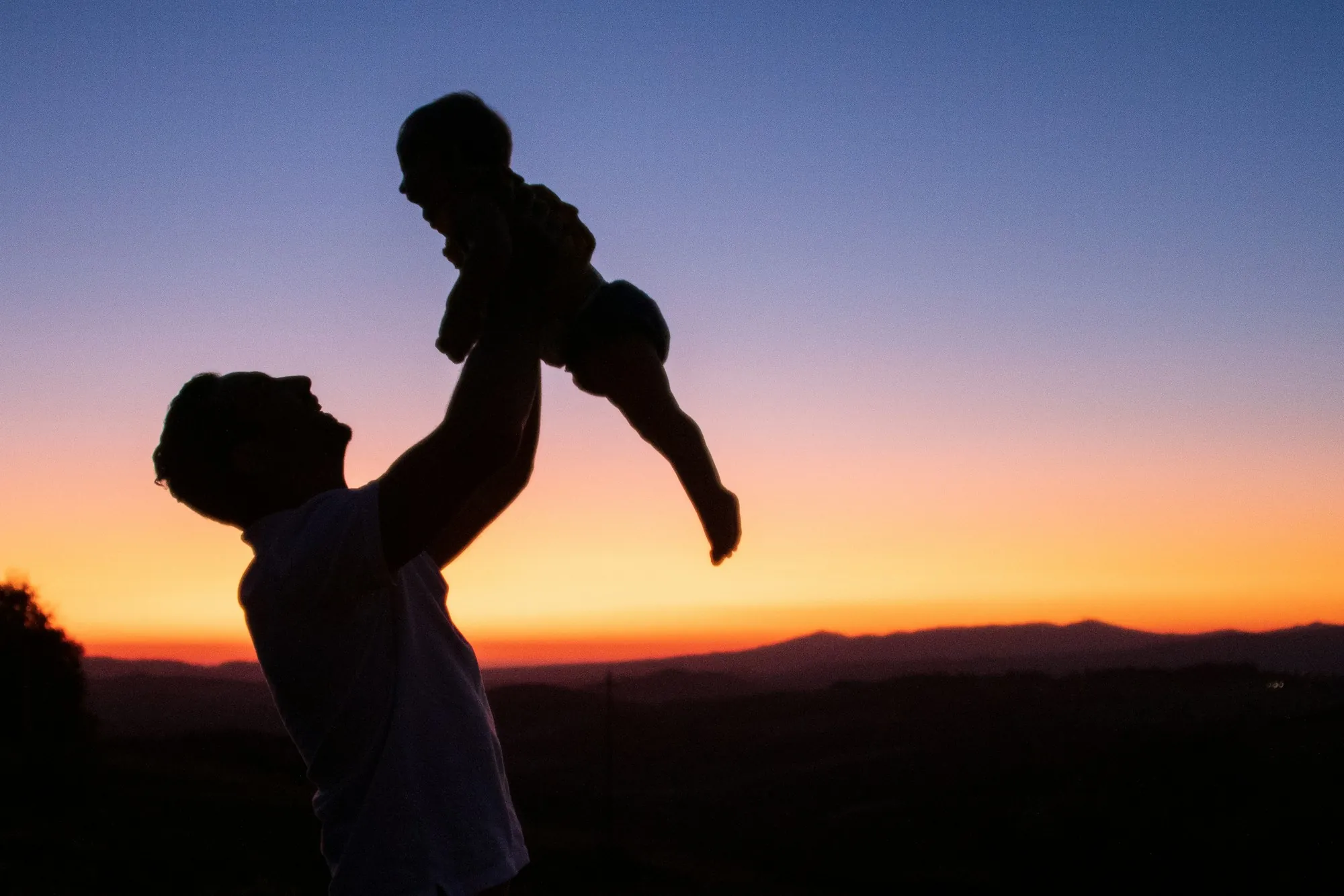 Silhouette of a parent lifting a baby at sunset